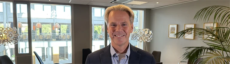 Forskare Thomas Andersson har ljust hår, rutig skjorta och mörk kavaj, han står i en loungemiljö