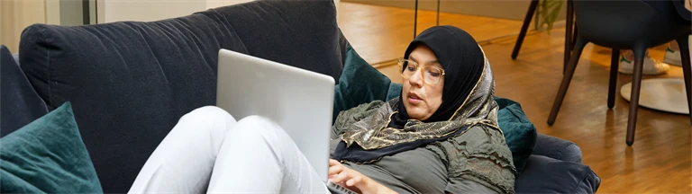 En person ligger i en soffa och arbetar med datorn.