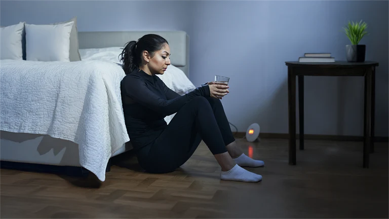 Kvinna i träningskläder sitter på golv lutad mot säng