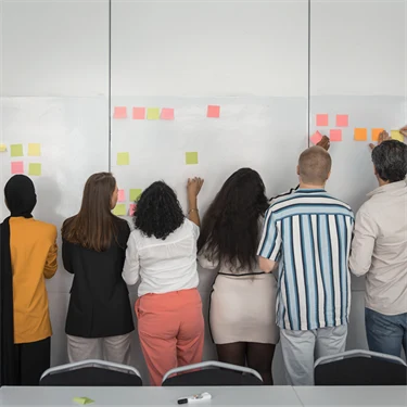 Medarbetare arbetar med post-it-lappar på stor tavla, planering, idéarbete eller visualisering