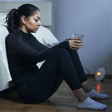 Kvinna i träningskläder sitter på golv lutad mot säng