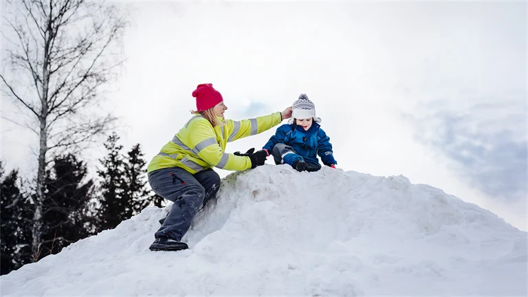 Försskolepedagog hjälper litet barn uppe på en snöhög