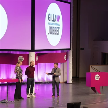 Två män och en kvinna på en stor scen inleder  arbetsmiljöeventet Gilla Jobbet 2022 i Folkets hus i Stockholm.