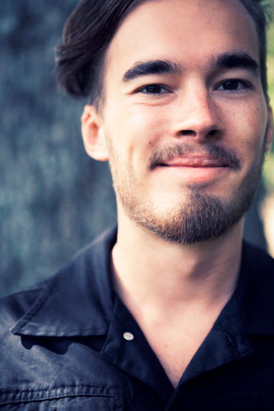 Man i svart skjorta framför en trädstam