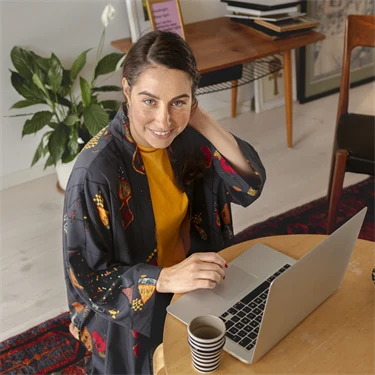 Kvinna sitter framför ett runt bord med en laptop och ett stearinljus.
