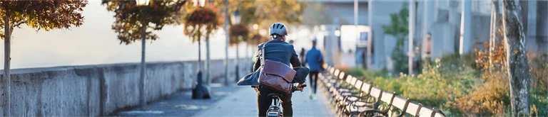 Man i kavaj cyklar med datorväska hängandes över ryggen