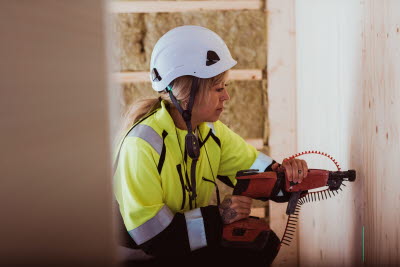 Kvinnlig byggnadsarbetare borrar i väggen