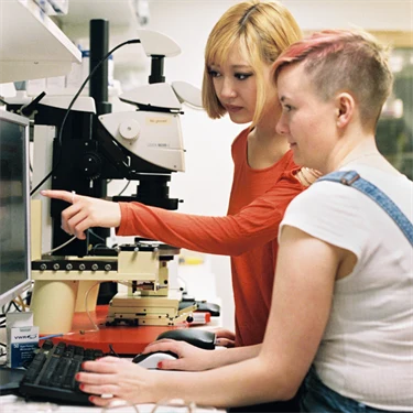 Två unga personer i ett laboratorium jobbar vid en dator.