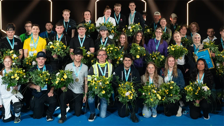 Gruppbild av alla guldmedaljörer i Yrkes-SM 2026, med medalj runt halsen och blombukett i handen.