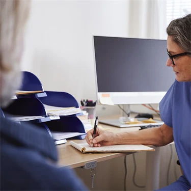 Patient på läkarbesök, där läkaren sitter och antecknar under besöket.