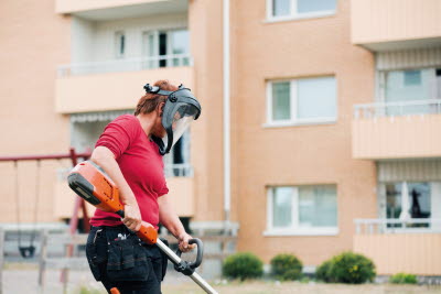 Kvinnlig parkarbetare i skyddsmask använder trimmer