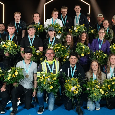 Gruppbild av alla guldmedaljörer i Yrkes-SM 2026, med medalj runt halsen och blombukett i handen.