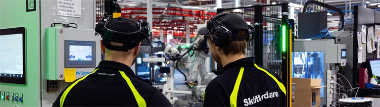 Två anställda på ROL Group tittar ut över fabriksmiljön. ROL Group har sökt och fått stöd för arbetsmiljöutbildning.