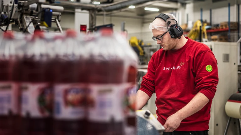 En person arbetar i produktionen i Spendrups fabrik. Personen har en röd tröja, glasögon och hörselkåpor på sig. 