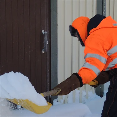 En person skottar snö utanför ett hus.