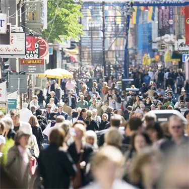 Folkträngsel på Drottninggatan, där världens nationers flaggor hänger på rader mellan husen.