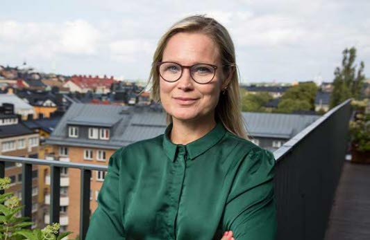 Porträttbild på Susanne Ribrant, vd för Prevent. Ribrant står på en balkong med utsikt över takåsar, och småler och tittar in i kameran. 