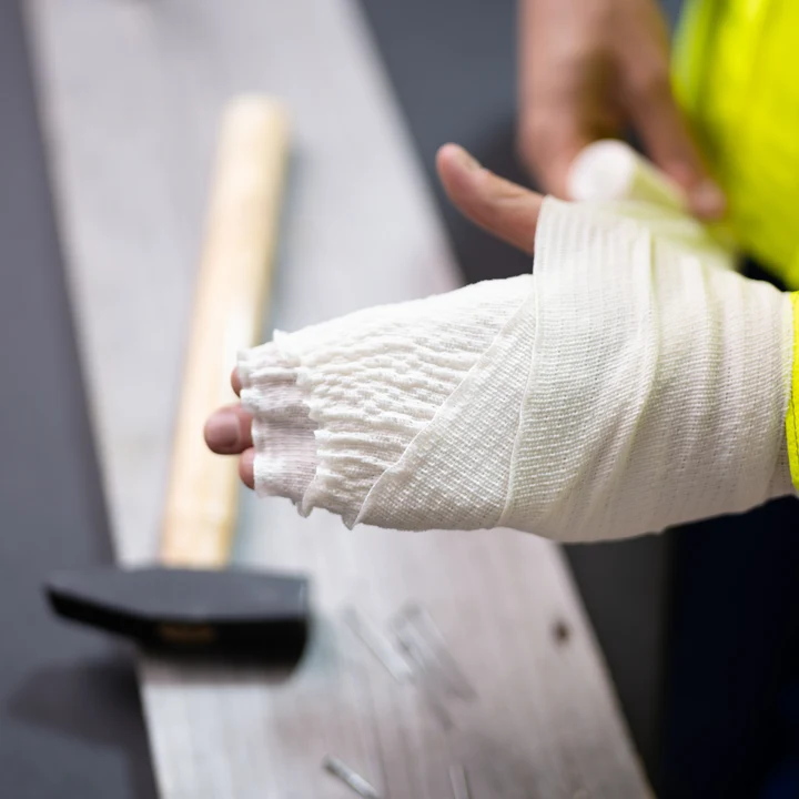 Person lindar bandage runt ena handen. På bordet bredvid ligger en hammare.