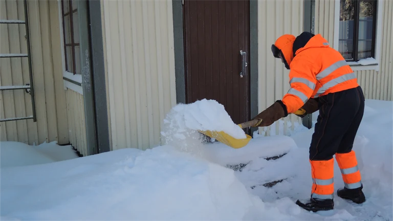 En person skottar snö utanför ett hus.