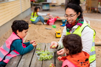 Förskolepersonal äter vindruvor med barnen utomhus