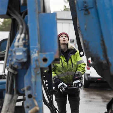 Kvinna i arbetskläder manövrerar stor maskin eller fordon med joystick eller liknande, 
