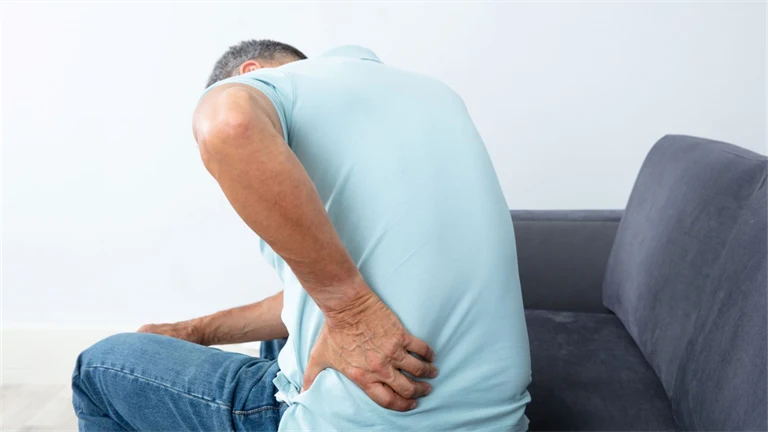 Sittande äldre man har ont i ryggen och tar sig om ländryggen.