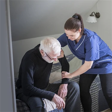 Kvinnlig vårdpersonal hjälper äldre man att resa sig från sin säng. 