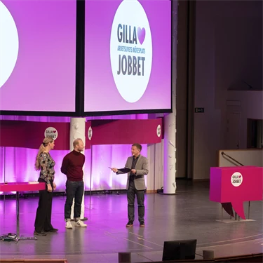 Två män och en kvinna på en stor scen inleder  arbetsmiljöeventet Gilla Jobbet 2022 i Folkets hus i Stockholm.
