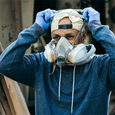 Man med skyddshandskar och bakåtvänd keps sätter på sig en skyddsmask