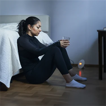 Kvinna i träningskläder sitter på golv lutad mot säng