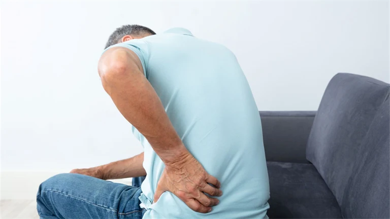Sittande äldre man har ont i ryggen och tar sig om ländryggen.