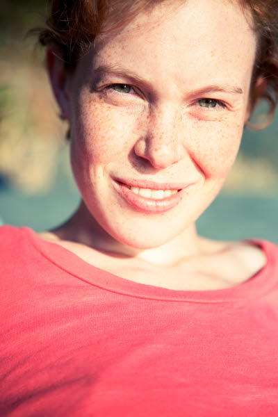 Fräknig kvinna med röd t-shirt kisar mot solen