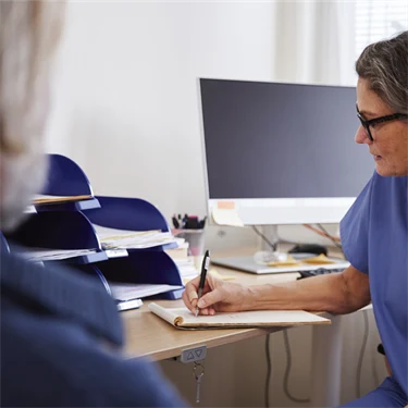 Patient på läkarbesök, där läkaren sitter och antecknar under besöket.