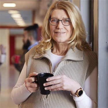 kvinna som står i skolkorridor med en kaffekopp i handen och ler mot kameran