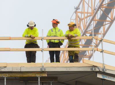 Tre byggjobbare i gula jackor står vid ett räcke