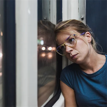 Kvinna med glasögon och blå t-shirt sitter på spårvagn och lutar huvudet mot fönstret