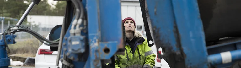 Kvinna i arbetskläder manövrerar stor maskin eller fordon med joystick eller liknande, 