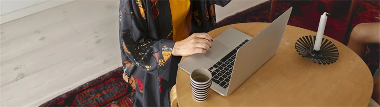 Kvinna sitter framför ett runt bord med en laptop och ett stearinljus.