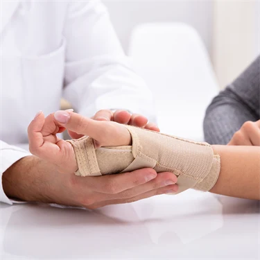 En kvinna får sin handled inlindad i bandage av en doktor.