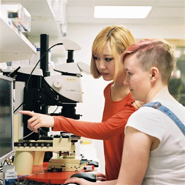 Två unga personer i ett laboratorium jobbar vid en dator.