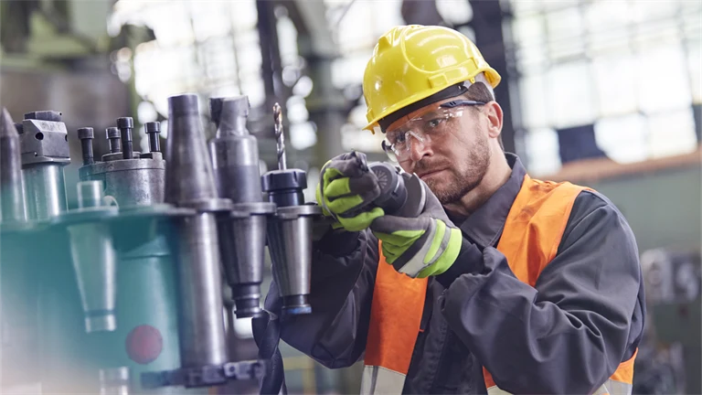Man i skyddskläder undersöker något i fabrik eller verkstad