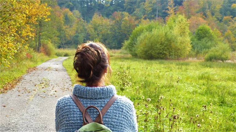 Halvbild bakifrån på en kvinna med ryggsäck som går mot en höstfärgad skog.