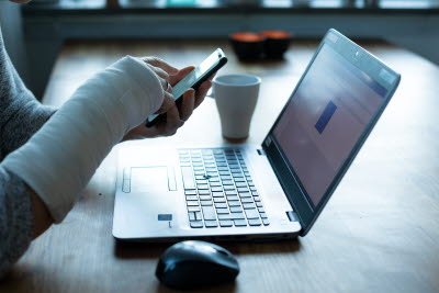 Skriver på dator och mobil med gipsad arm