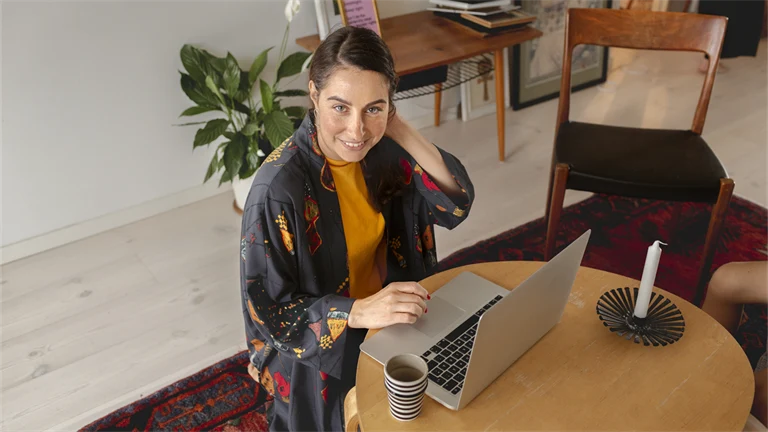 Kvinna sitter framför ett runt bord med en laptop och ett stearinljus.