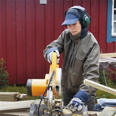 person som sågar till plankor utanför ett hus