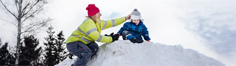 Försskolepedagog hjälper litet barn uppe på en snöhög