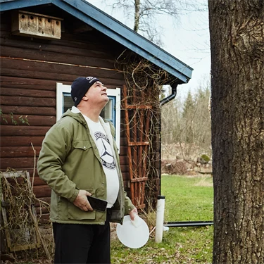 person står nedanför ett träd utanför en stuga