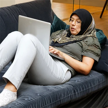 En person ligger i en soffa och arbetar med datorn.