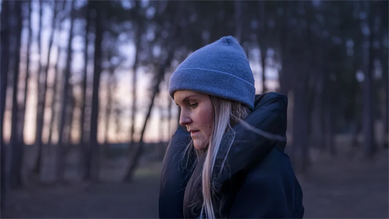 Kvinna med mössa på skogspromenad i skymning eller gryning