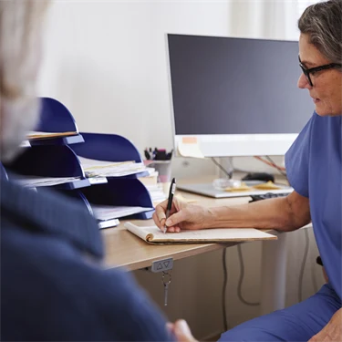 Patient på läkarbesök, där läkaren sitter och antecknar under besöket.